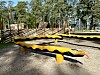 Svart og gult lekeapparat på en utendørs lekeplass med trær i bakgrunnen.
